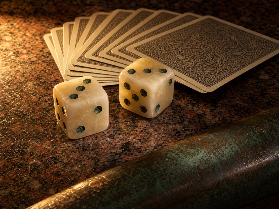 Due dadi in alabastro con puntini in rame patinato accanto a un ventaglio di carte da gioco coperte, su una lastra di granito rosso di Assuan.